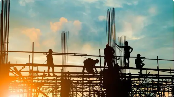 Siluetas de trabajadores en una construcción durante el atardecer.